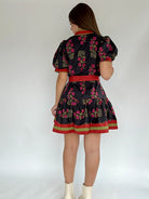 Woman wearing a black floral dress with a red belt on a white background showing back view