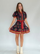 Woman wearing a black floral mini dress with a red belt and short sleeves against a plain background