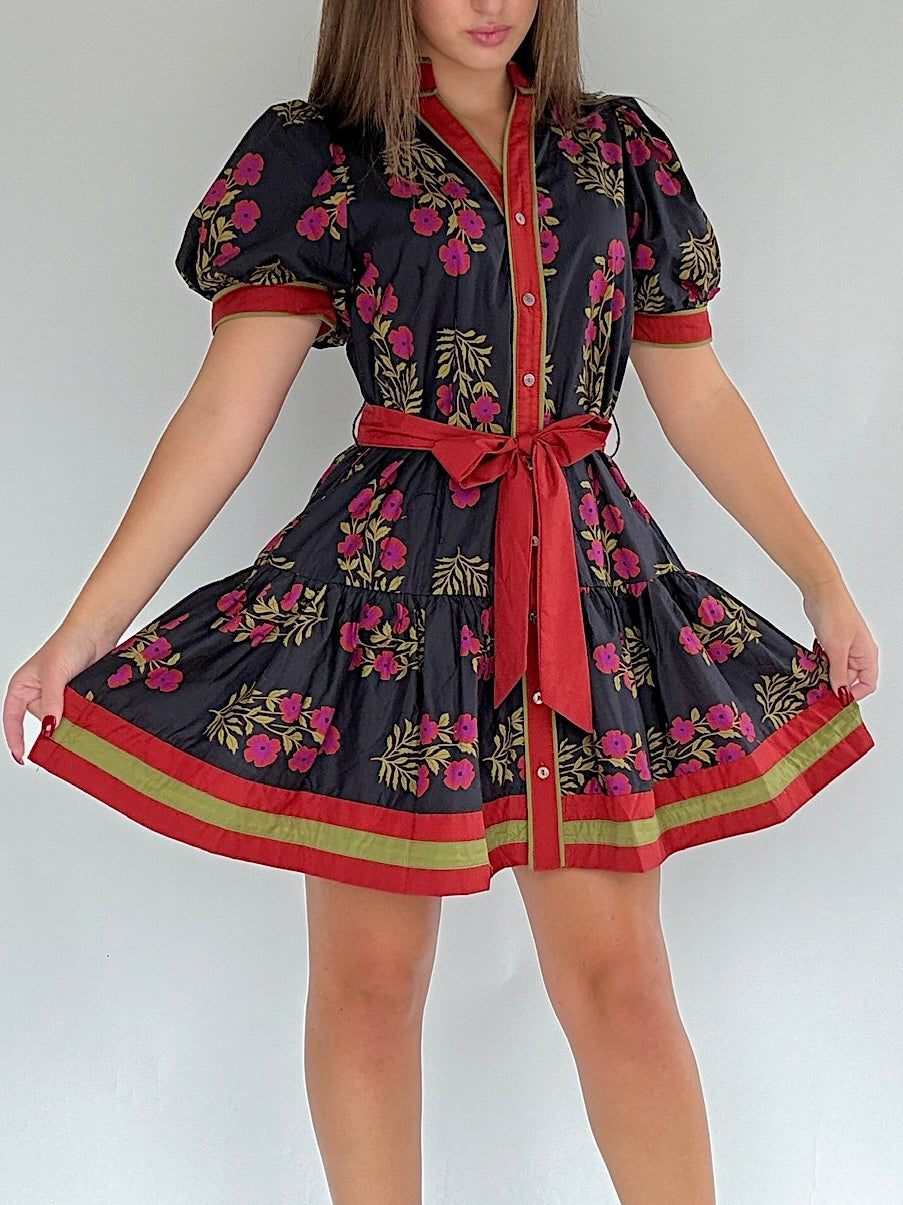 Woman wearing a floral dress with a red belt, button front and short puff sleeves on a white background