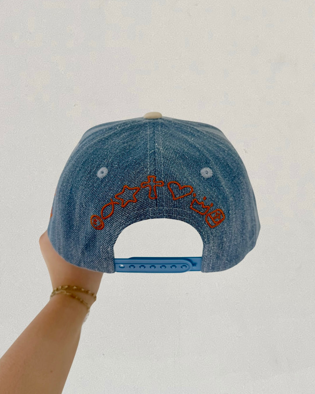 Denim cap with embroidered design held by a hand against a plain background