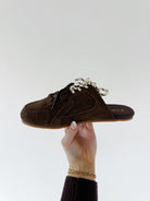 Brown suede sneaker mule shoe held by a hand against a white background