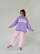 Person wearing a purple 'Dilly Dally' sweatshirt and pink checkered pants on a plain background