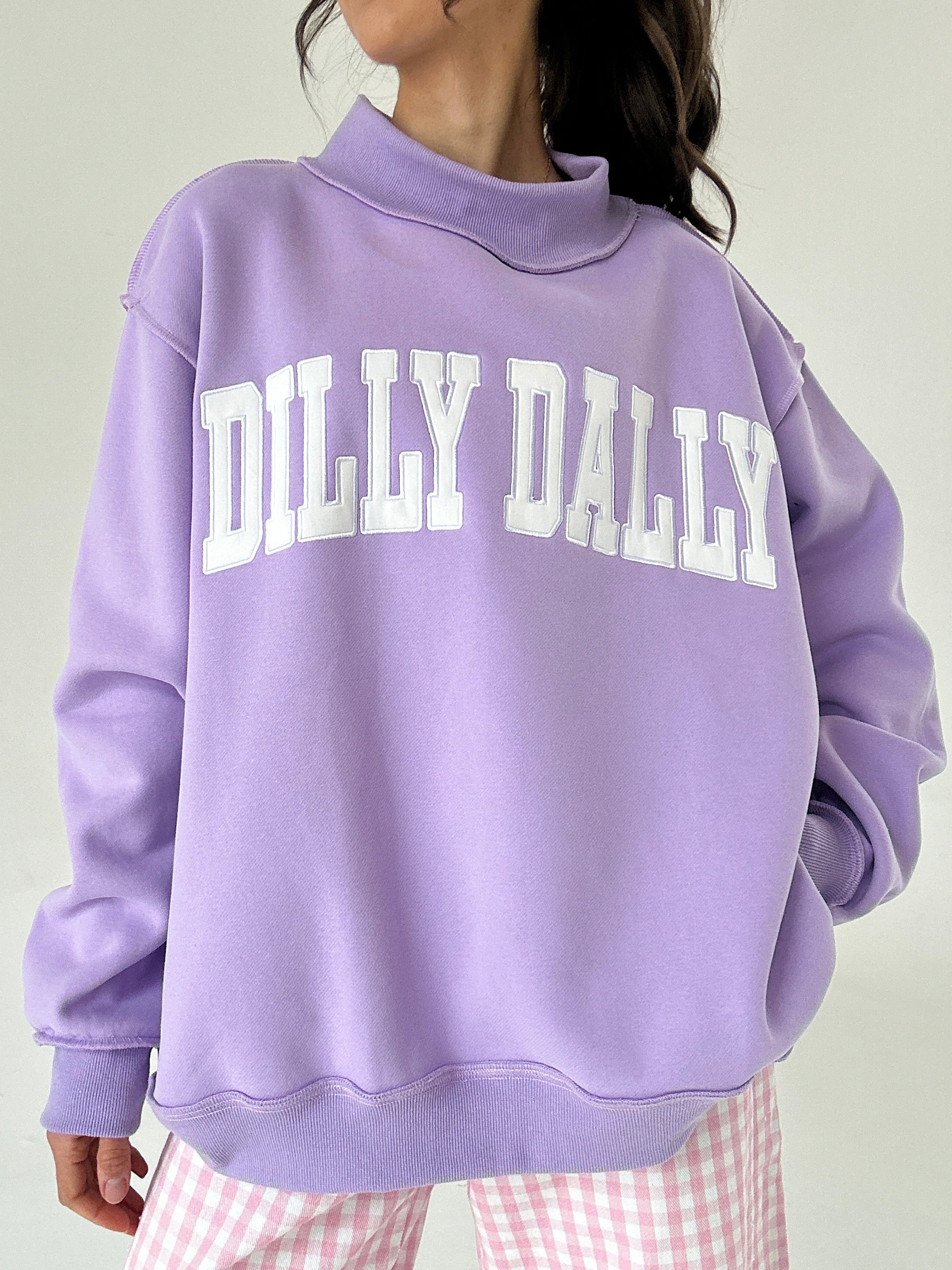 Person wearing a purple sweatshirt with 'Dilly Dally' text on a plain background