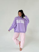 Woman wearing a purple 'Dilly Dally' hoodie and pink checkered pants on a white background