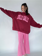 Person wearing a maroon mockneck pullover with pink 'DILLY DALLY' text and pink pants on a white background