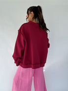 Person wearing a maroon sweatshirt and pink pants against a white background from back