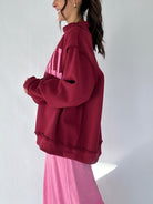 Person wearing a maroon mock neck with pink text on a white background from side