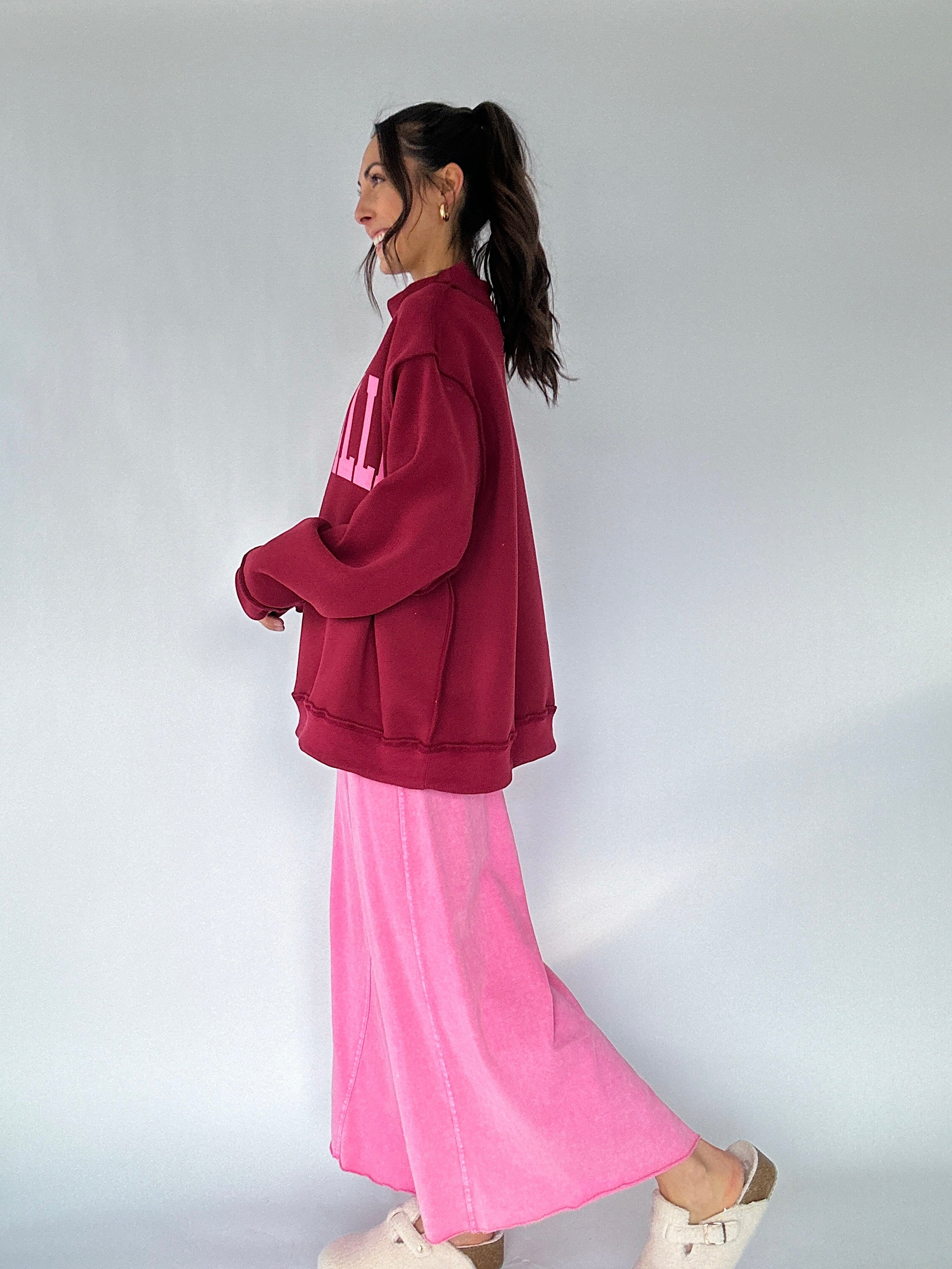 Person wearing a maroon mock neck and pink pants on a plain background from side