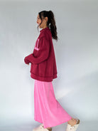 Person wearing a maroon mock neck and pink pants on a plain background from side