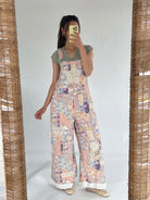 Person wearing a floral patchwork overalls over a green t-shirt taking a selfie in the mirror