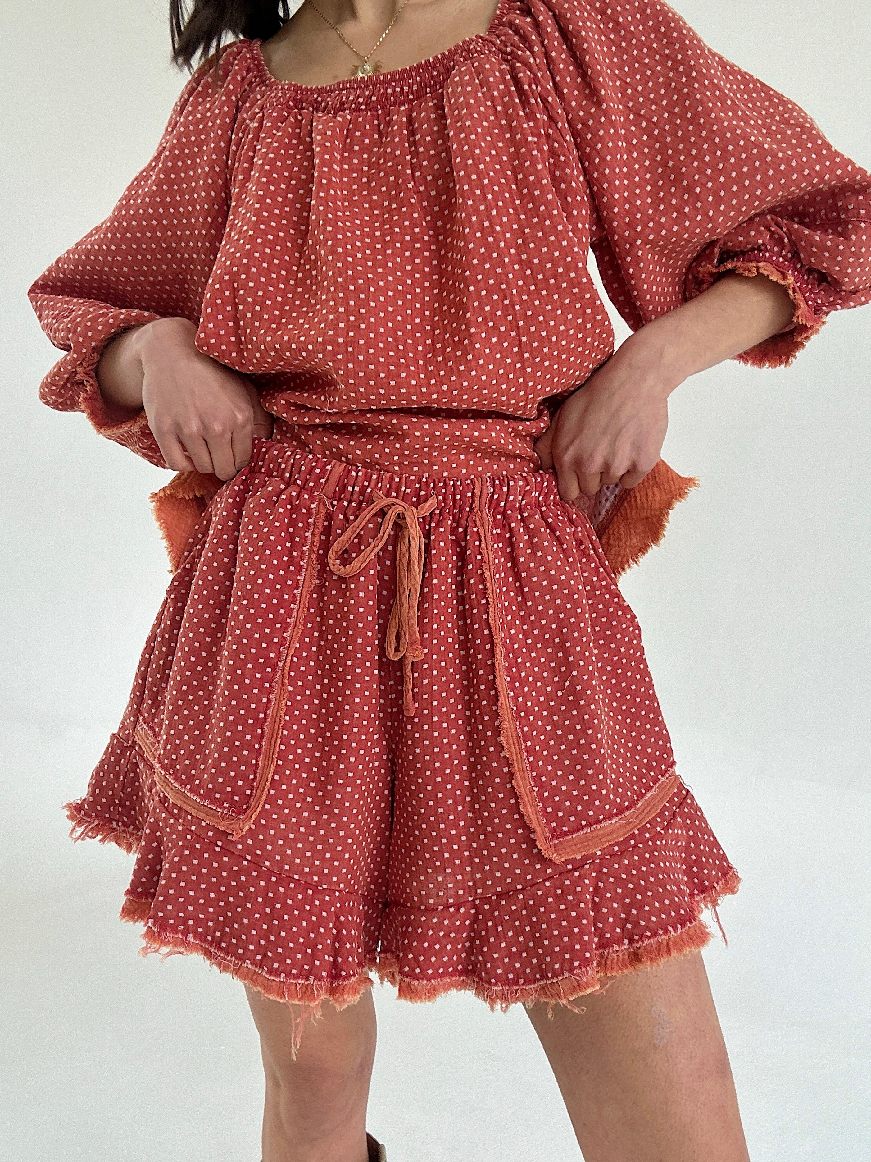 Person wearing a rust-colored polka dot set with ruffle shorts on a white background