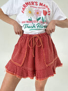 Person wearing a white t-shirt with floral graphics and text, paired with red polka dot shorts on a plain background.