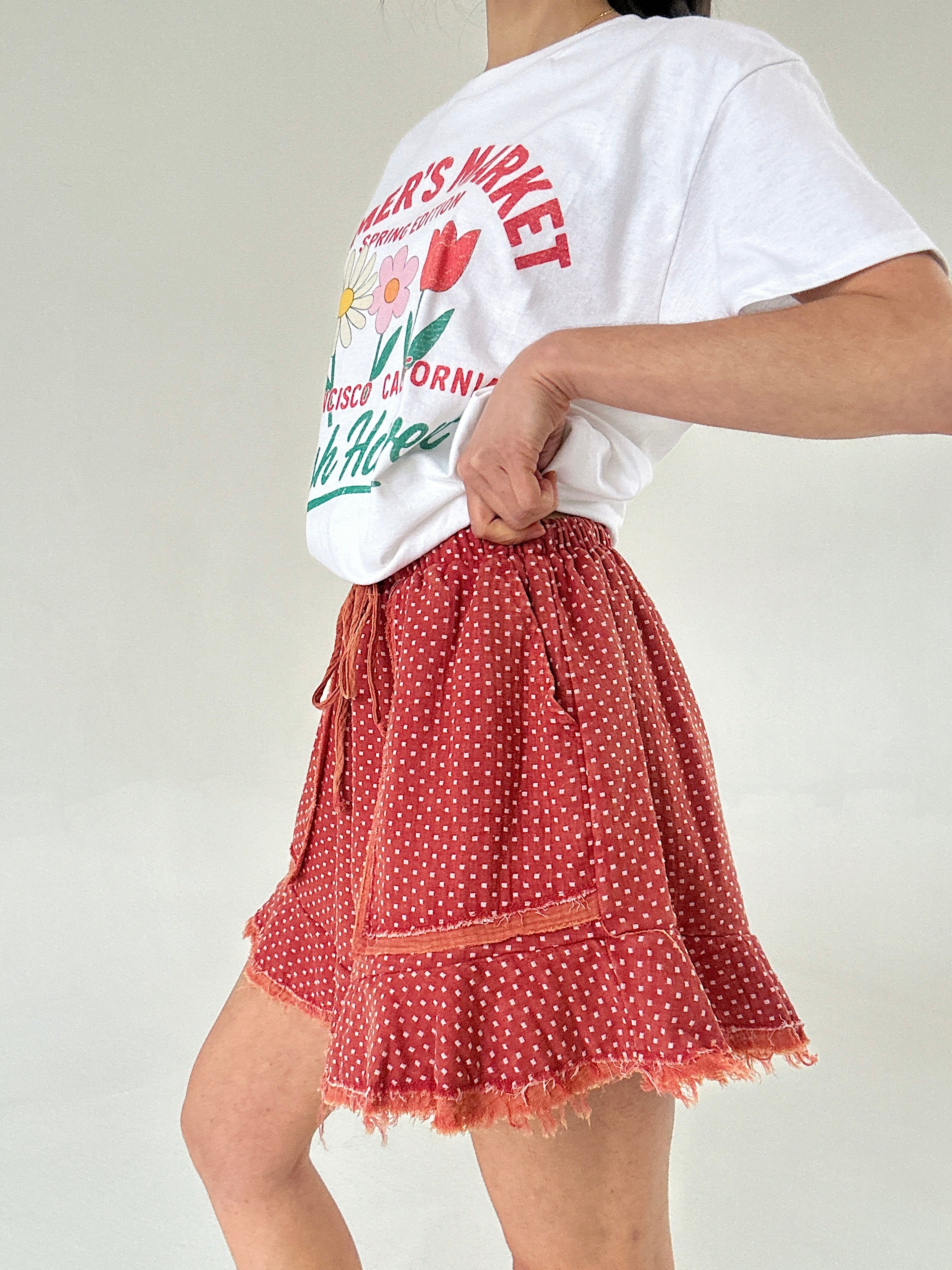 Person wearing a white t-shirt with graphics and a red polka dot short on a plain background