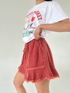 Person wearing a white t-shirt with graphics and a red polka dot short on a plain background