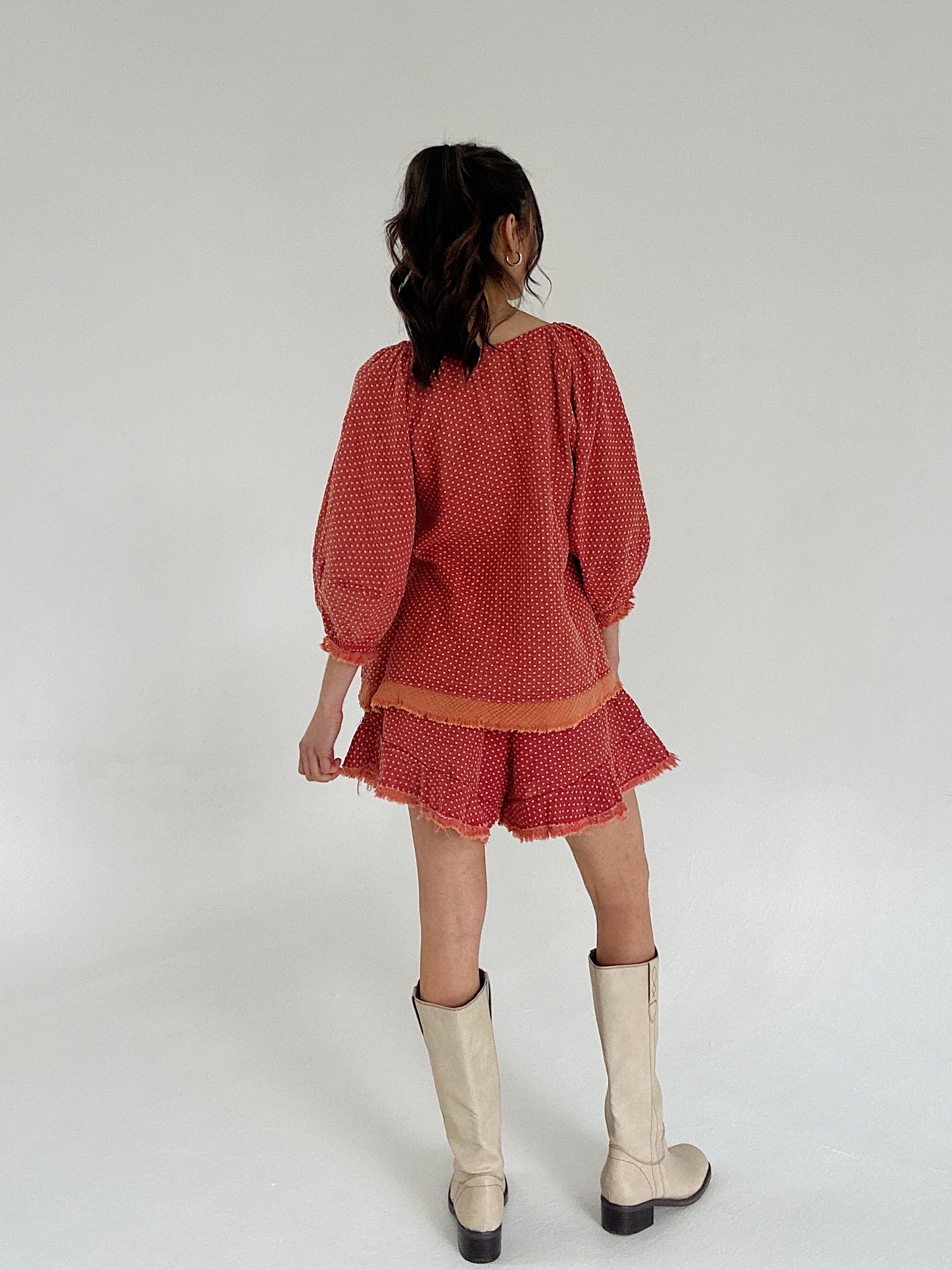 Person wearing a red dotted set with white boots on a plain background showing back