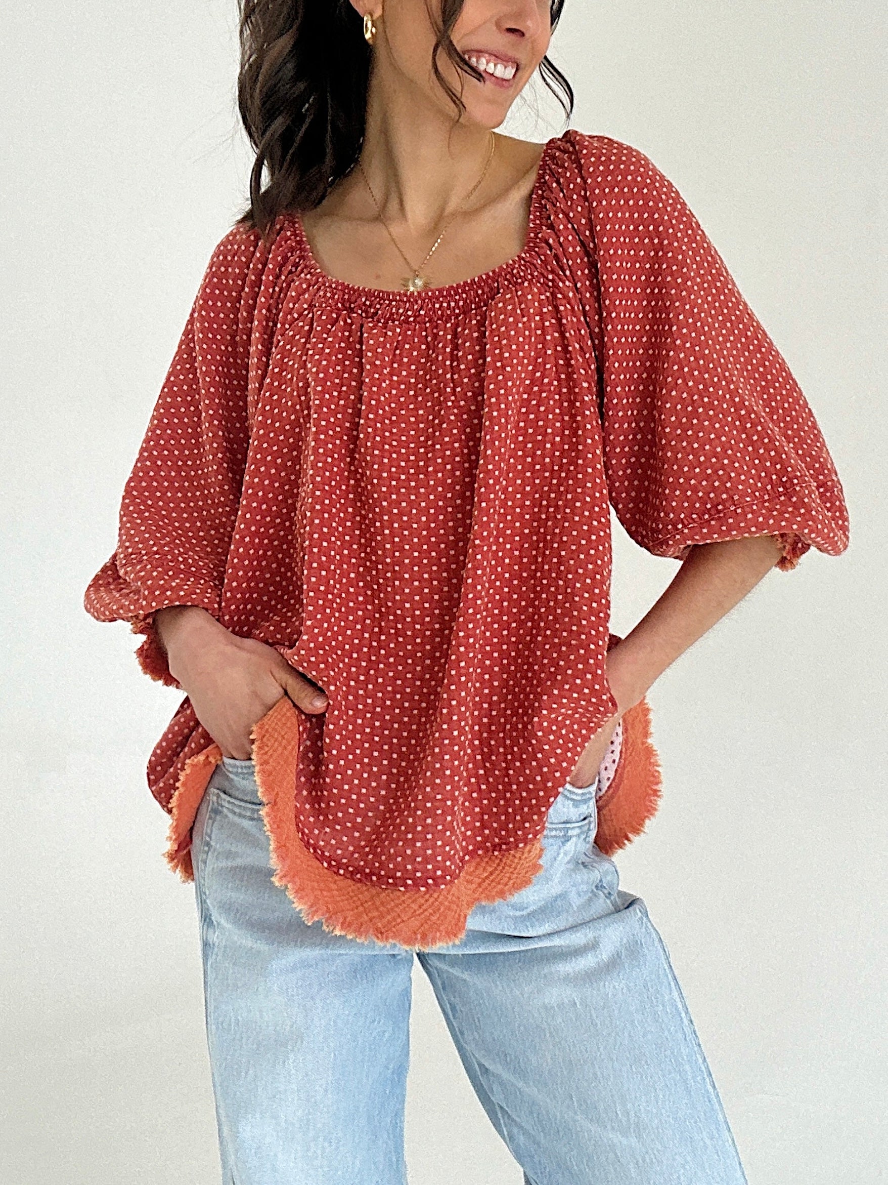Woman wearing a rust-colored blouse with white polka dots and light blue jeans against a plain background