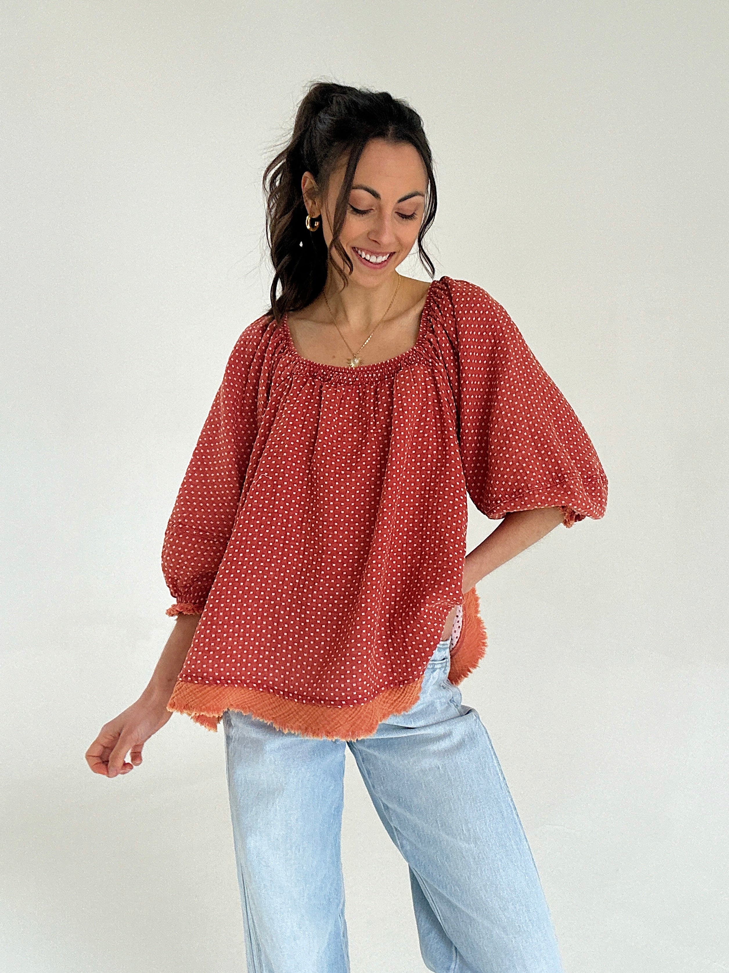 Woman wearing a red polka dot blouse and light blue jeans against a white background