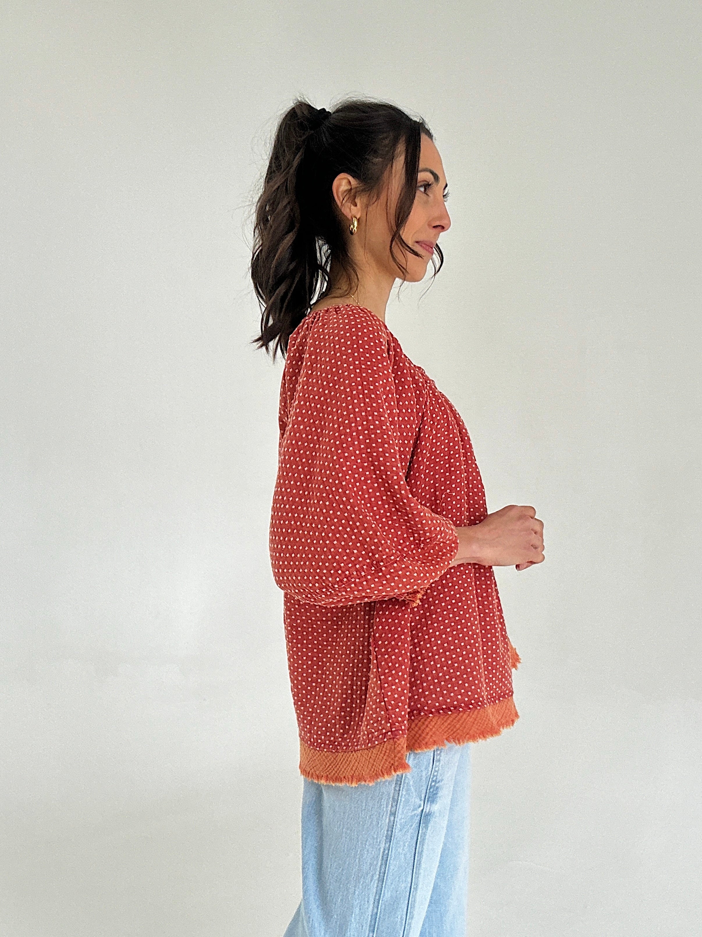 Woman wearing a red patterned top against a white background from side