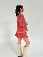 Woman wearing a red set with ruffled layers and white boots on a plain background