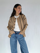 Woman wearing a beige striped cardigan with black buttons, white shirt, and blue jeans against a white background