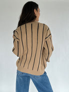 Person wearing a beige sweater with black stripes and blue jeans on a white background showing the back