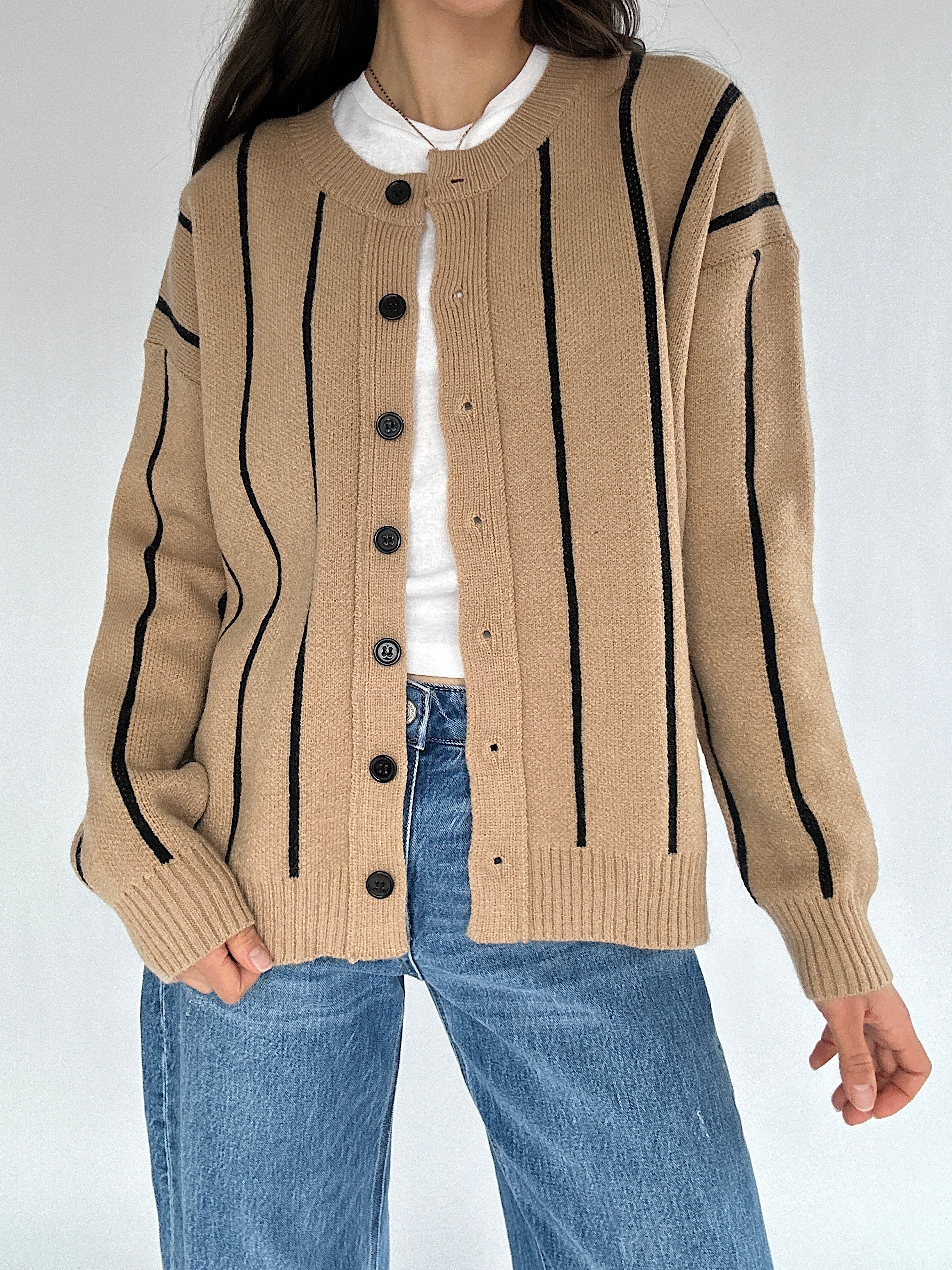 Person wearing a beige cardigan with black stripes and buttons on a white background