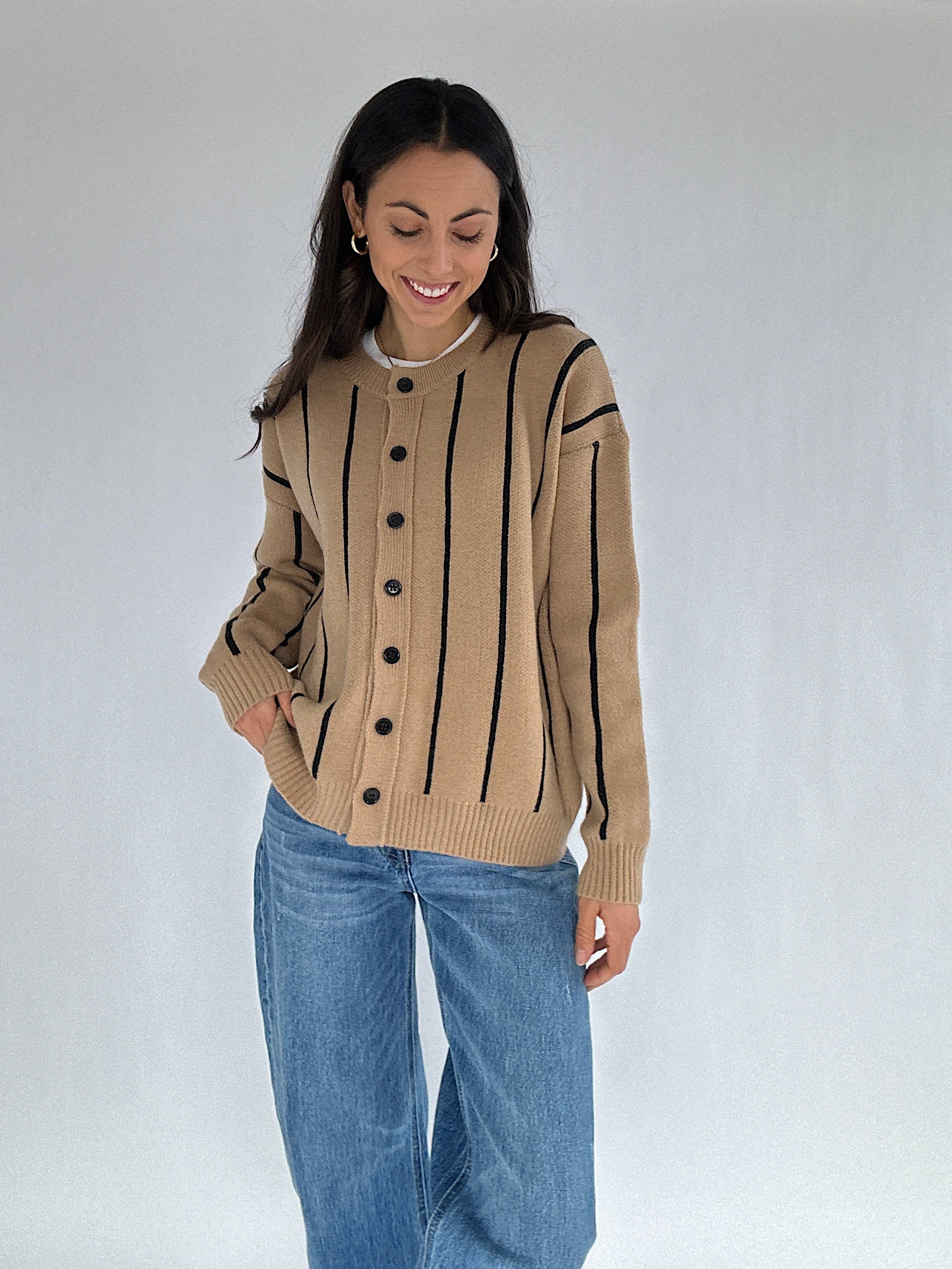 Woman wearing a beige cardigan with black stripes and blue jeans on a white background