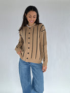 Woman wearing a beige cardigan with black stripes and blue jeans on a white background