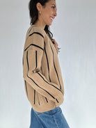 Woman wearing a beige sweater with black stripes against a white background showing the side
