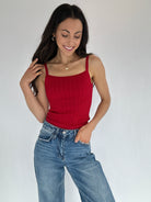 Woman wearing a red cable knit tank top and blue jeans against a plain background