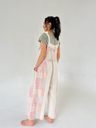 Woman wearing a floral overalls and green top on a plain background from back