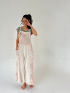 Woman wearing a floral overall jumper over a plain shirt and pants on a white background