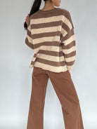 Person wearing a brown and beige striped sweater with brown pants on a white background from back