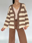 Person wearing a brown and beige striped cardigan unbuttoned on a plain background
