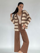 Woman wearing a brown and beige striped cardigan with brown pants on a white background