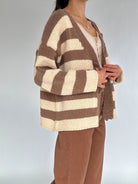 Person wearing a brown and beige striped cardigan on a plain background from side