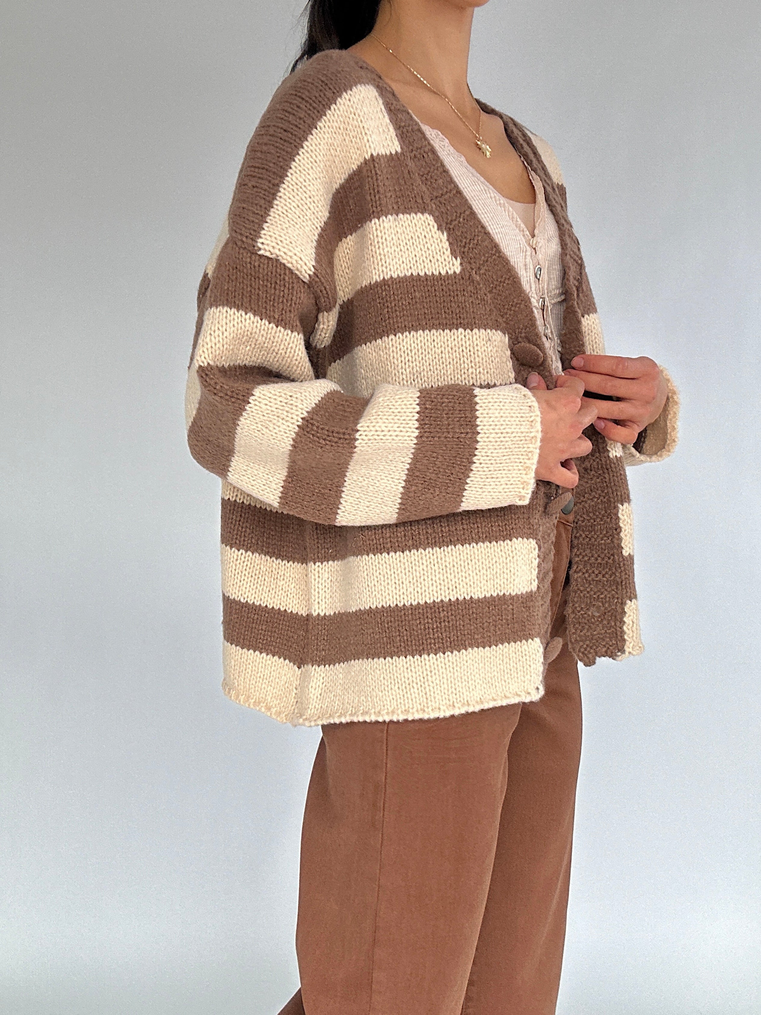 Person wearing a brown and beige striped cardigan on a plain background from side