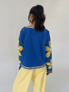 Person wearing a blue pullover with yellow floral patterns and yellow pants against a plain background