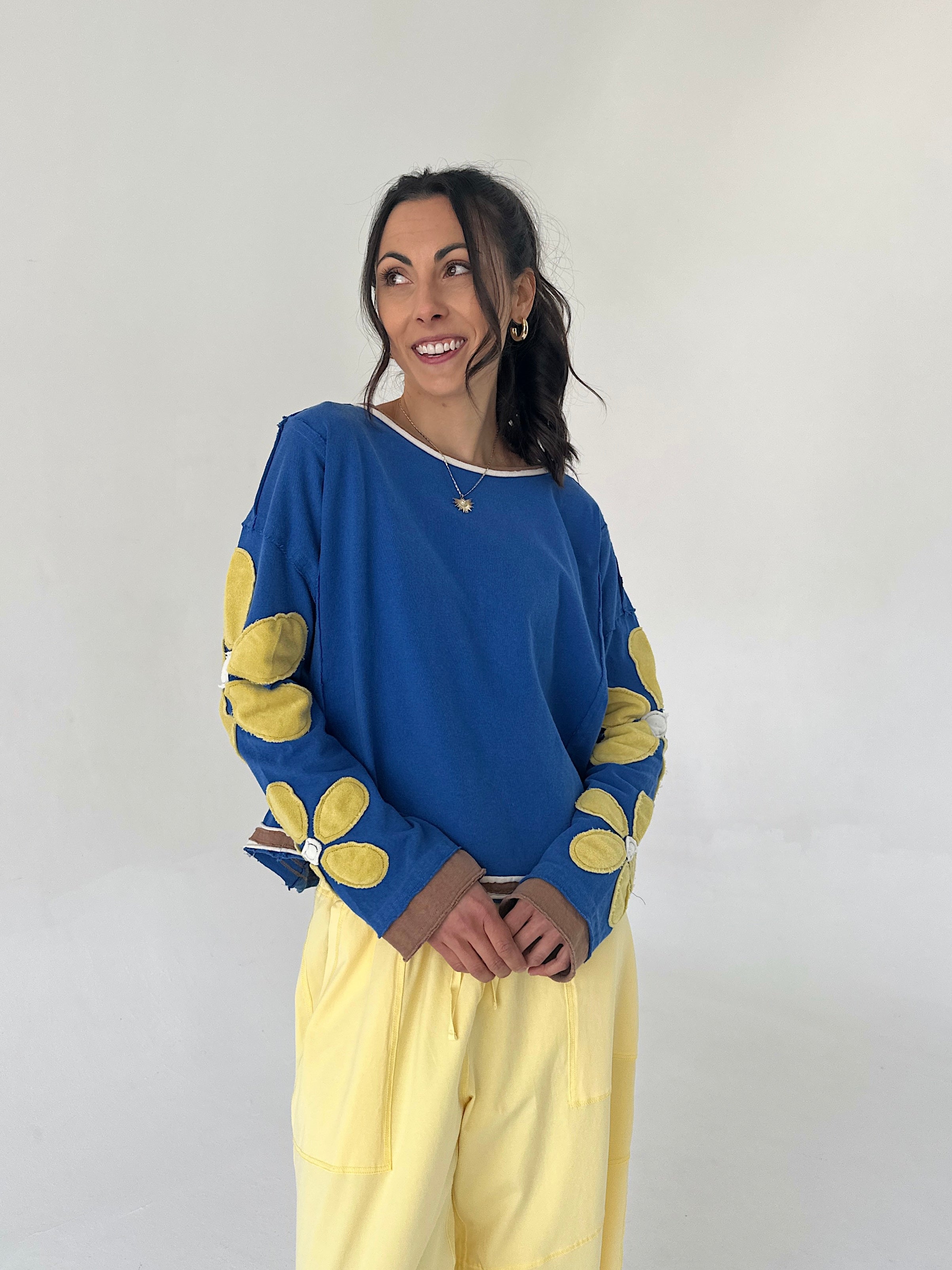 Woman wearing a blue sweater with yellow flower patterns and yellow pants against a white background
