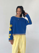 Woman wearing a blue sweater with yellow polka patches and yellow pants against a white background