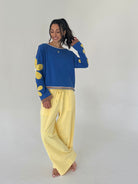 Woman wearing a blue top with yellow patterns and yellow pants on a plain background