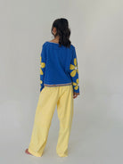 Person wearing a blue top with yellow floral patterns and yellow pants on a plain background