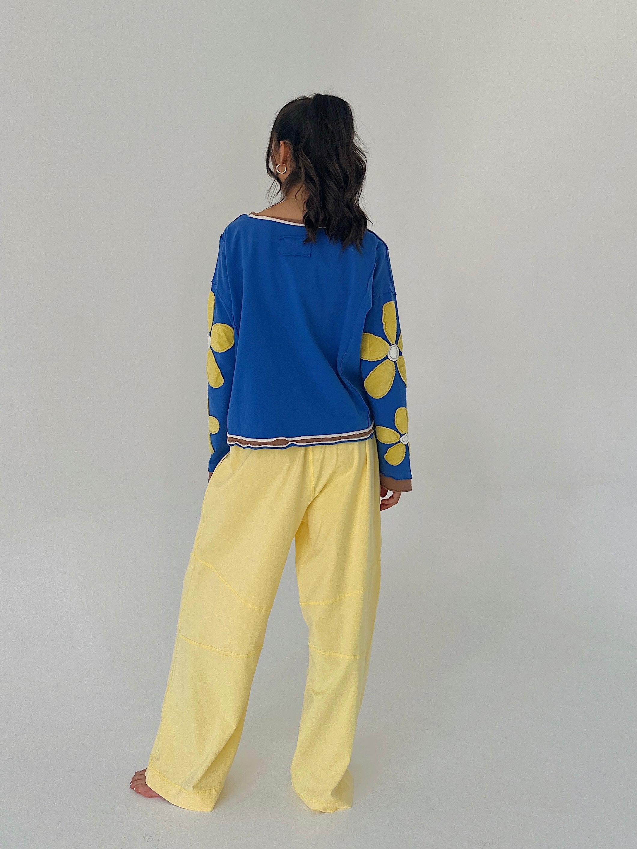 Person wearing a blue top with yellow floral patterns and yellow pants on a plain background