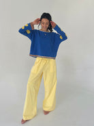 Woman wearing a blue sweater with yellow accents and yellow pants on a plain background