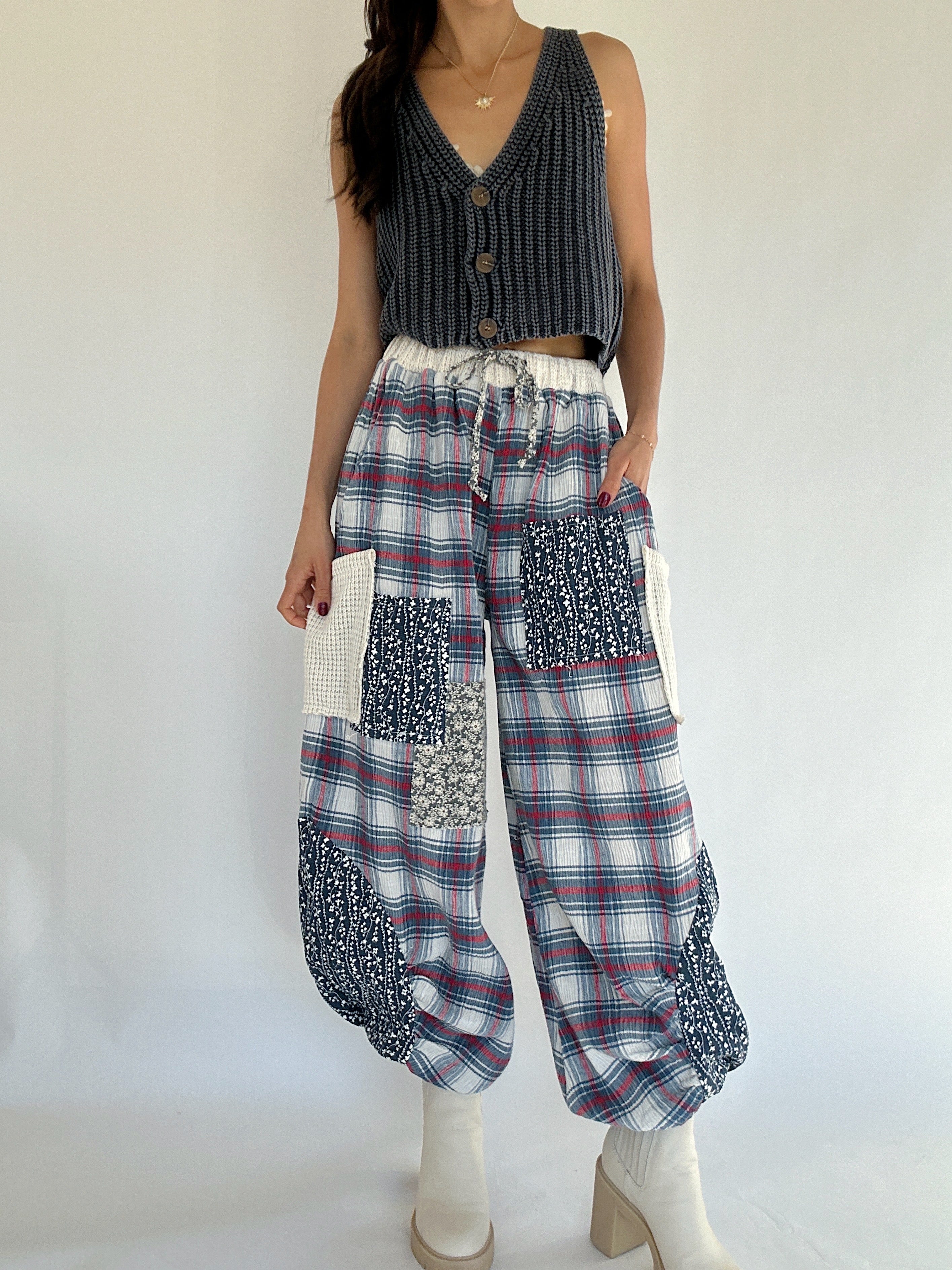 Person wearing a navy knit vest top and plaid jogger style pants with patchwork on a white background