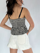 Person wearing a black and white patterned top and white shorts on a plain background - back of tank