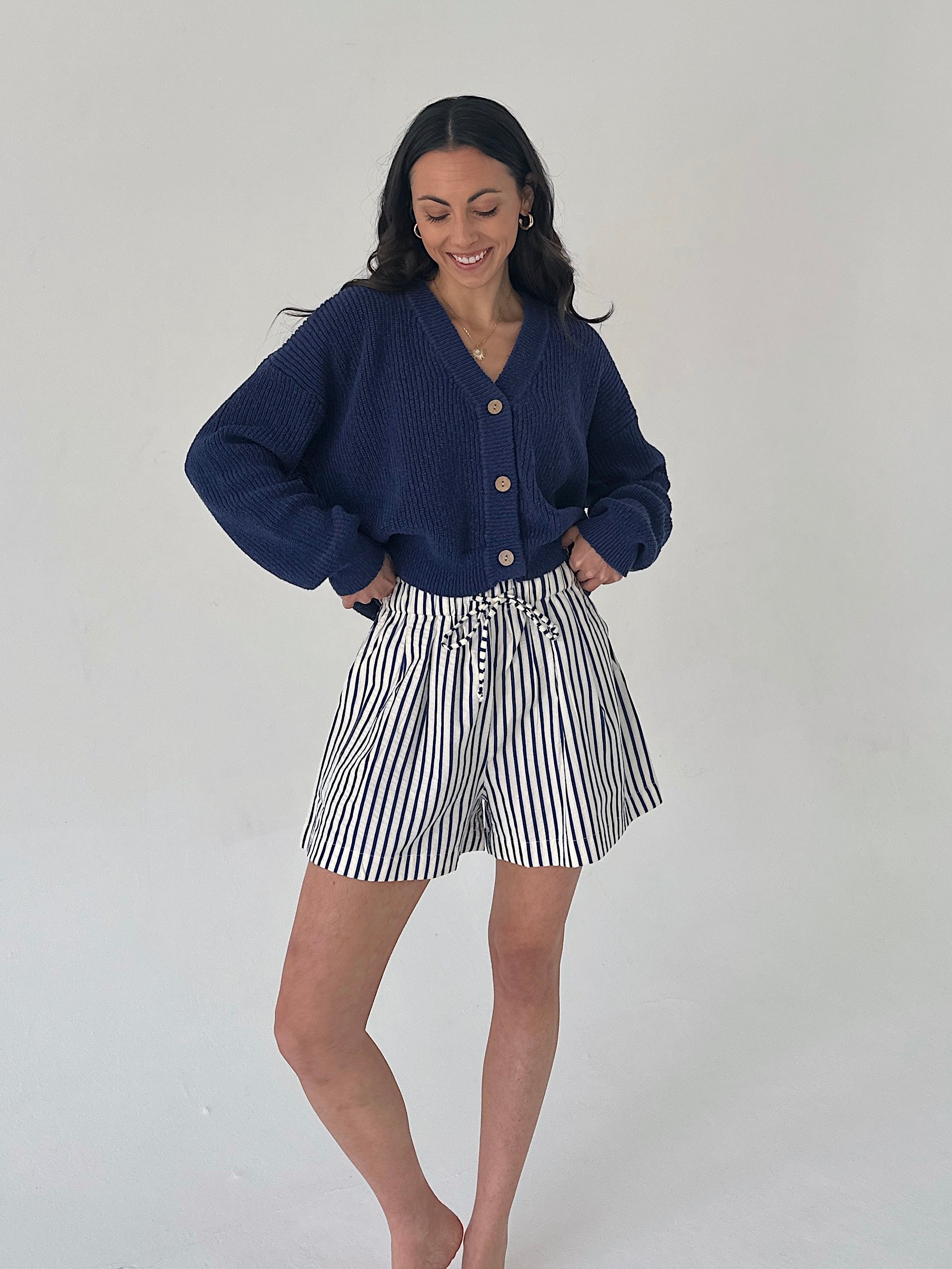 Woman wearing a navy cardigan and striped shorts on a plain background