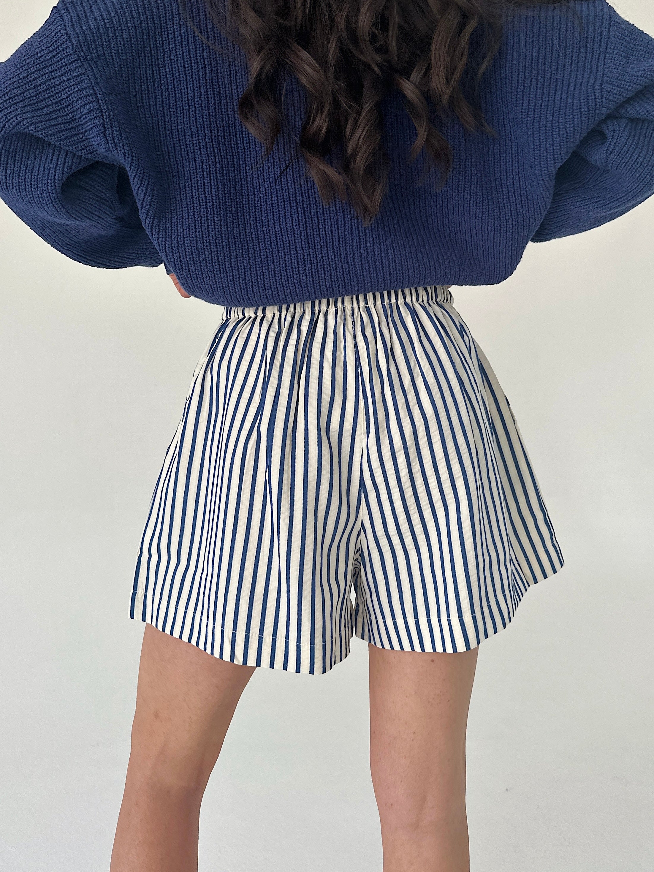 Person wearing blue sweater and striped shorts on a plain background from back