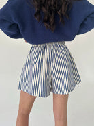 Person wearing blue sweater and striped shorts on a plain background from back