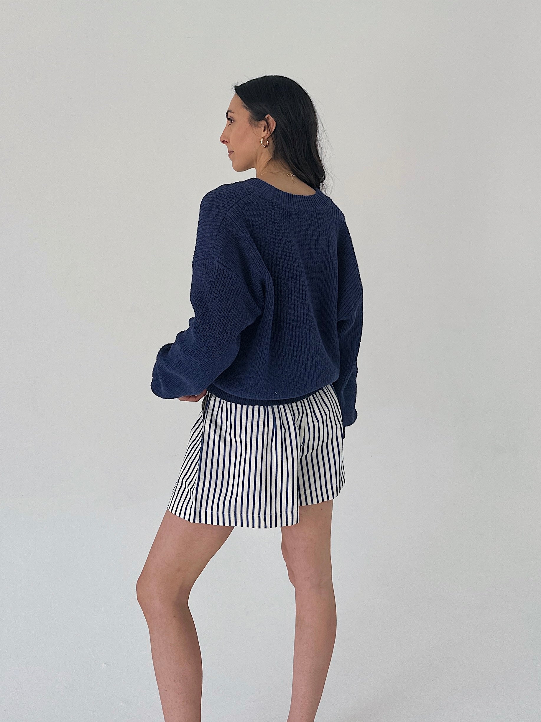 Woman wearing a navy sweater and striped skirt on a plain background
